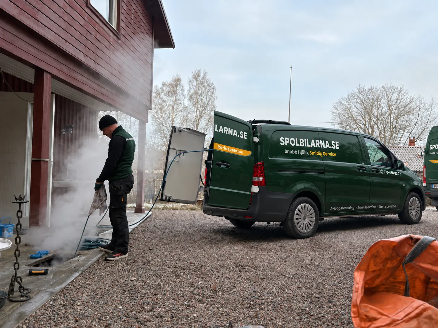 Tekniker från Spolbilarna spolar ett avlopp med hetvatten vid en villa, med spolbilen parkerad bredvid – Spolbilarna i Trollhättan