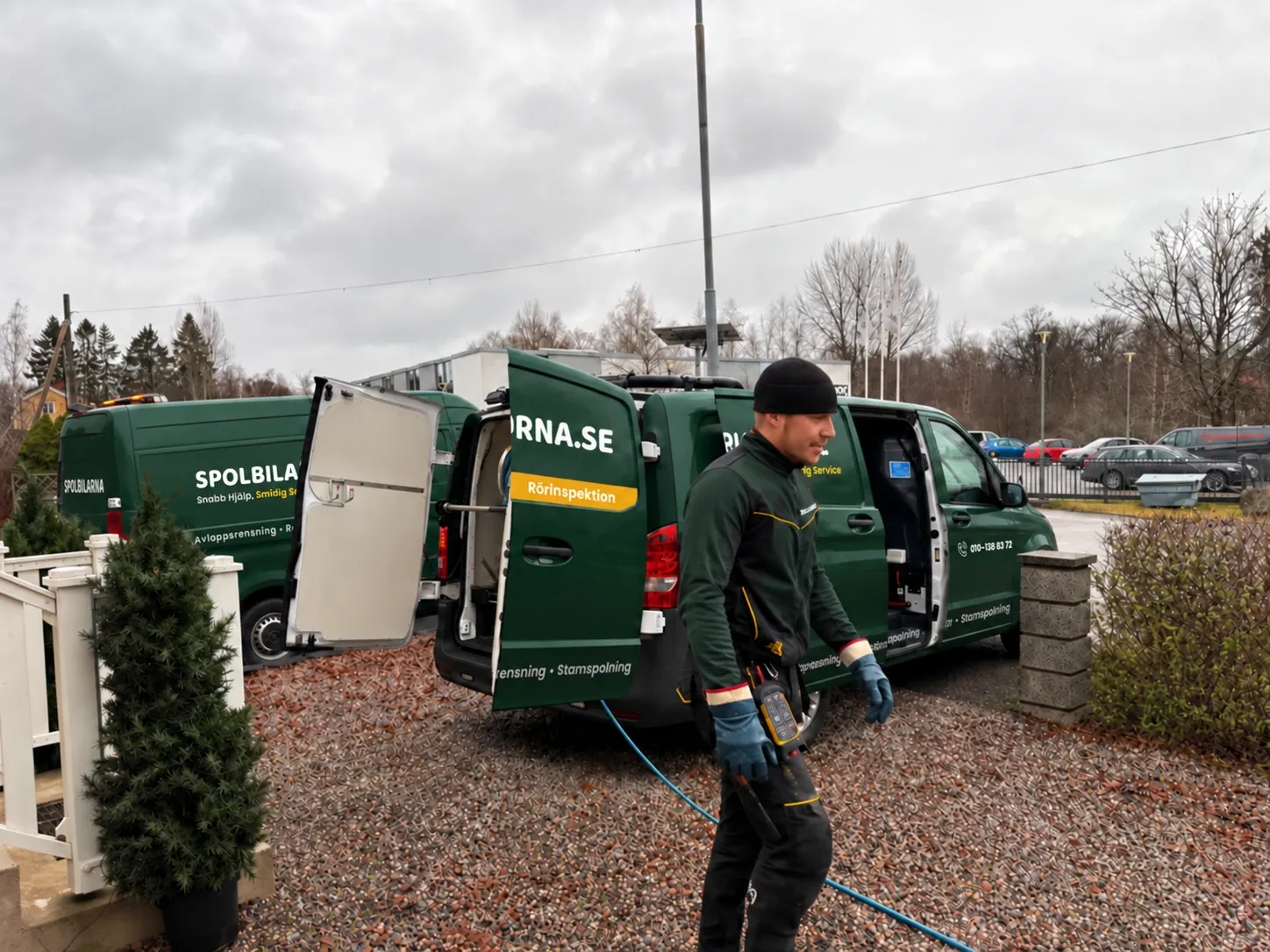 Tekniker från Spolbilarna på väg till ett uppdrag, med spolbilarna i bakgrunden – Spolbilarna i Alingsås